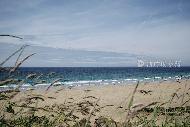 6月的一天，阳光明媚，康沃尔郡纽基市的菲斯特拉尔海滩上，穿过野草看到蓝色的大海、沙滩和蓝天。