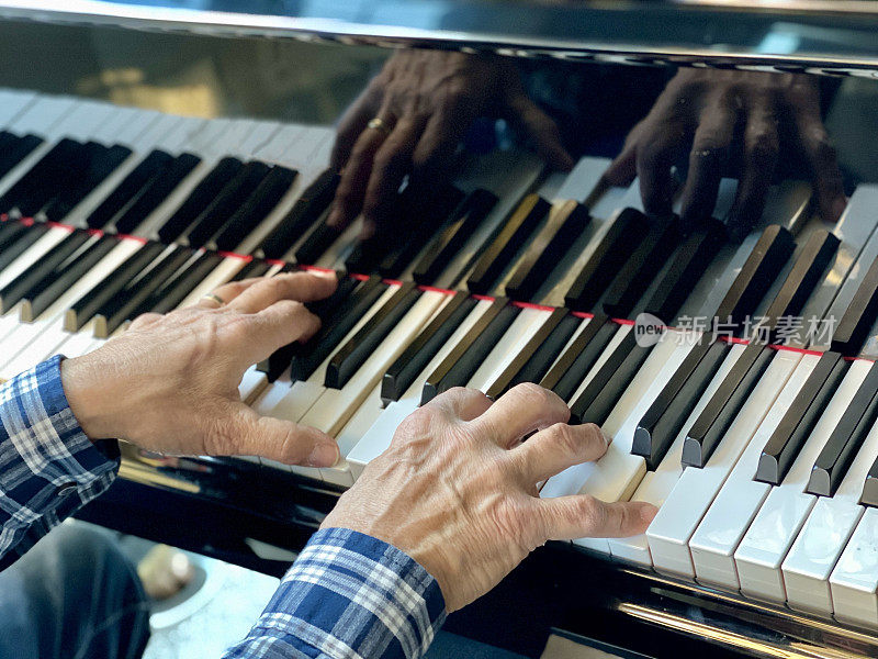 老人的手和他弹奏时在钢琴上的倒影