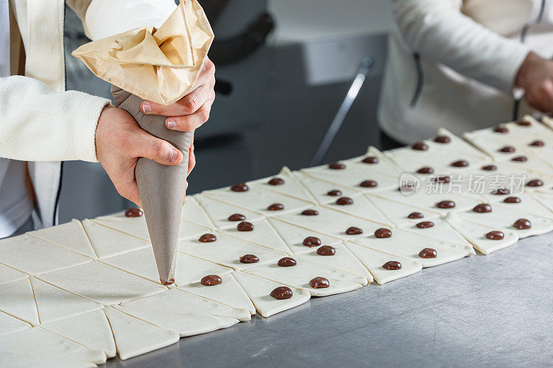 用裱花袋和挤压巧克力奶油滴在三角形面团块