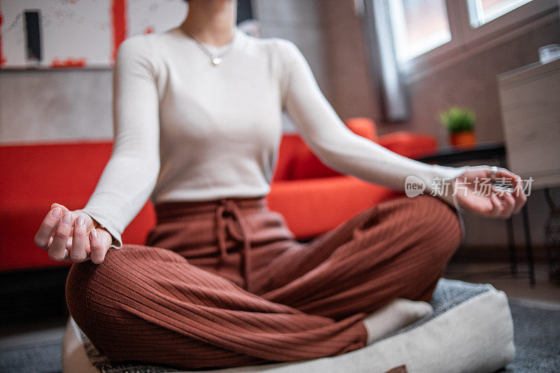 一名年轻女子坐在家里的地板上练习瑜伽或冥想，缓解压力