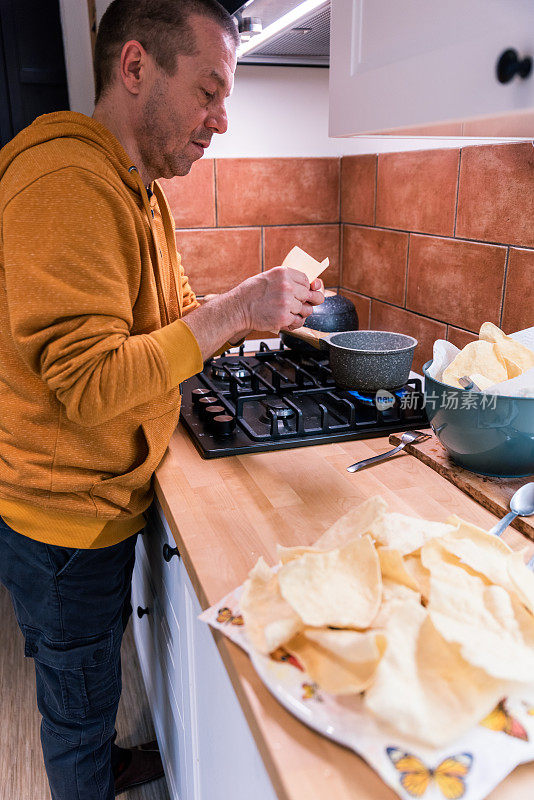 一个成熟的男人在家里的厨房里煎着传统的印度小吃——帕帕多姆