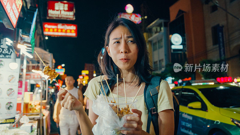 年轻的亚洲女性背包客在泰国曼谷的夜市享受街头小吃。假日度假旅行。