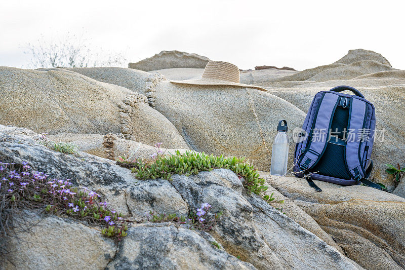 哈尔基季基上,在你的春天徒步旅行。背包、帽子和可重复使用的塑料瓶放在海滩附近的岩石上