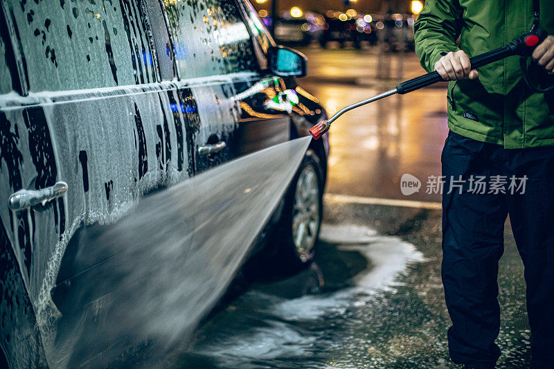 一名男子在自助洗车店用带加压水的软管洗车
