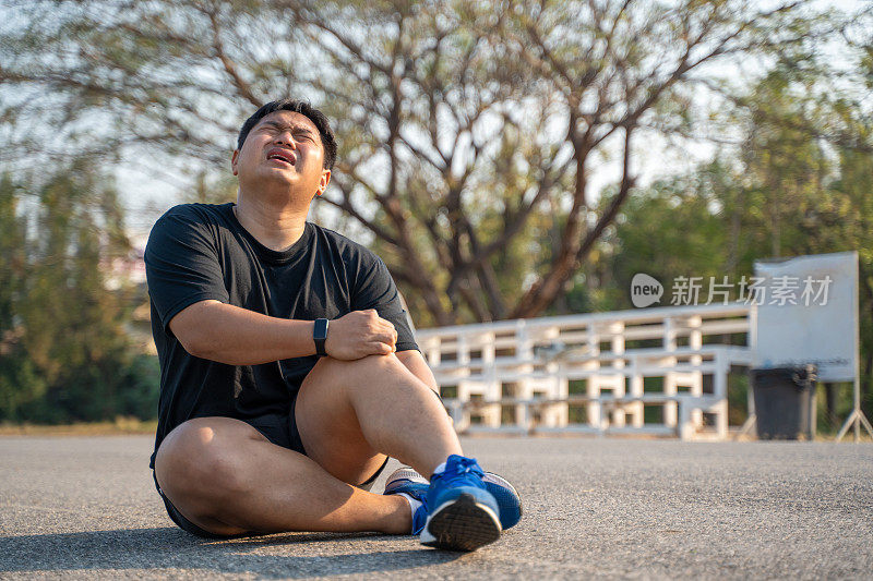 一个年轻人在跑步公园晨跑时，坐在地上抓着自己的膝盖和腿，感到疼痛