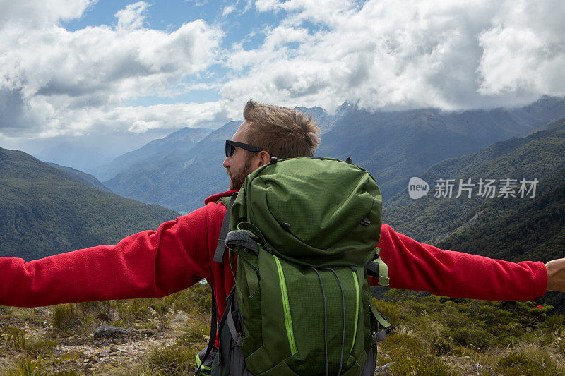 年轻人在山顶上张开双臂，享受自由