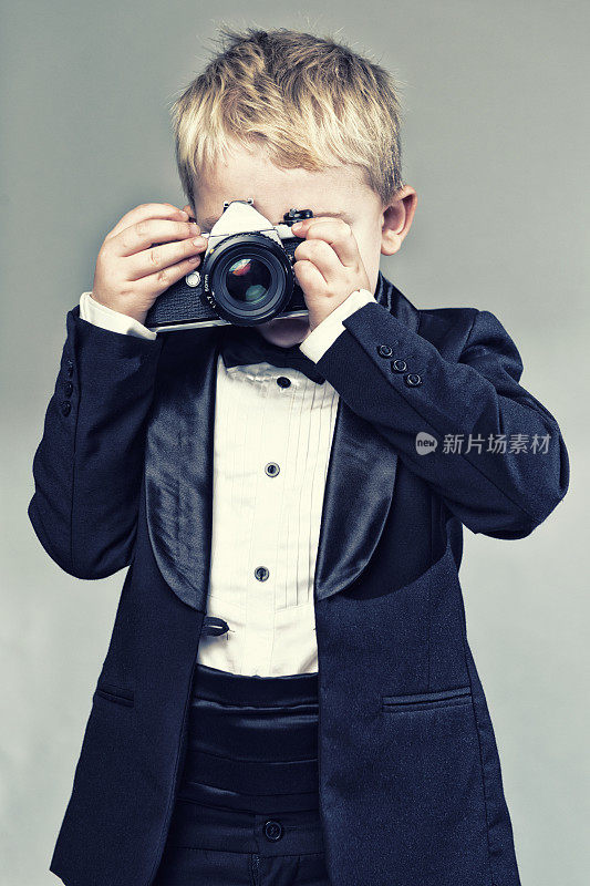 穿着燕尾服的男孩用老式复古相机拍照