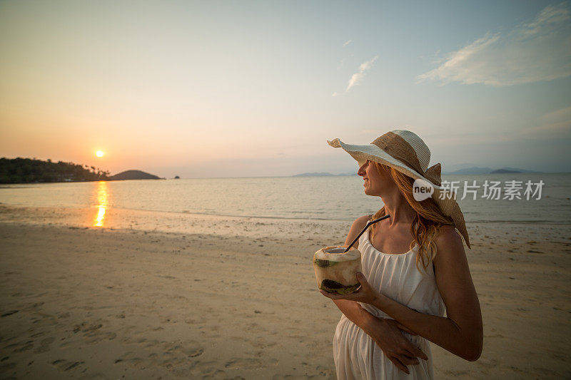美丽的女人和椰子在日落的海滩上