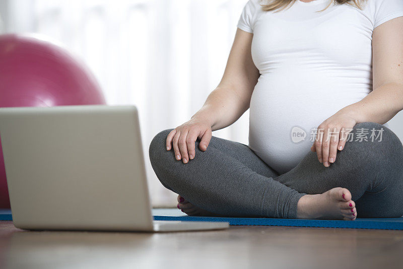 孕妇在笔记本电脑前做瑜伽