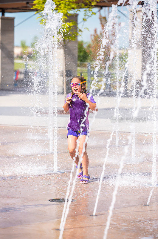 女孩在户外水花公园的喷泉中奔跑