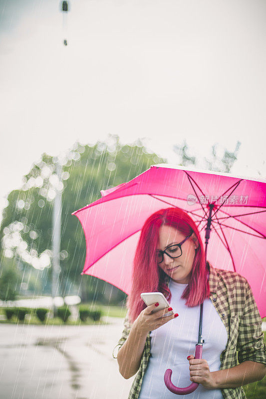 拿着雨伞在街上看手机的女人。