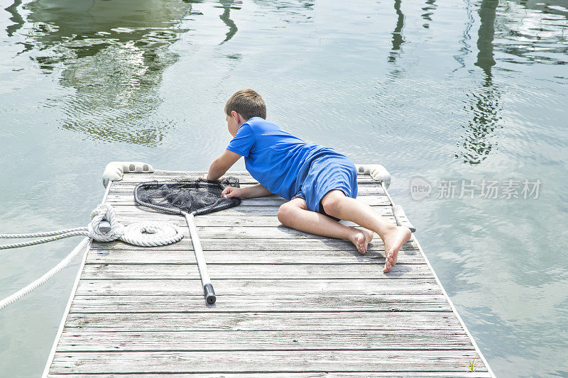 一个白人男孩躺在码头上，用渔网向下看