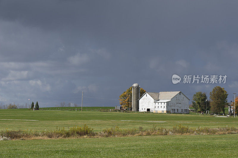 遥远的黑暗雨穿过农场，阳光下的白色谷仓，天气