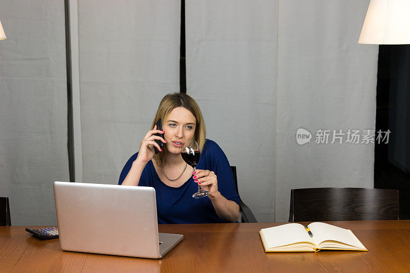 漂亮的女商人在办公室里用电脑和手机喝酒。