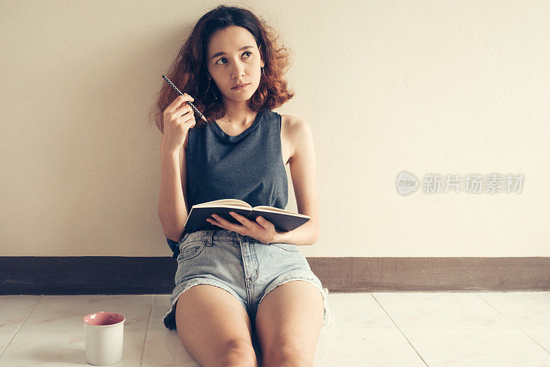 年轻女子坐在家里的地板上写书。的语气