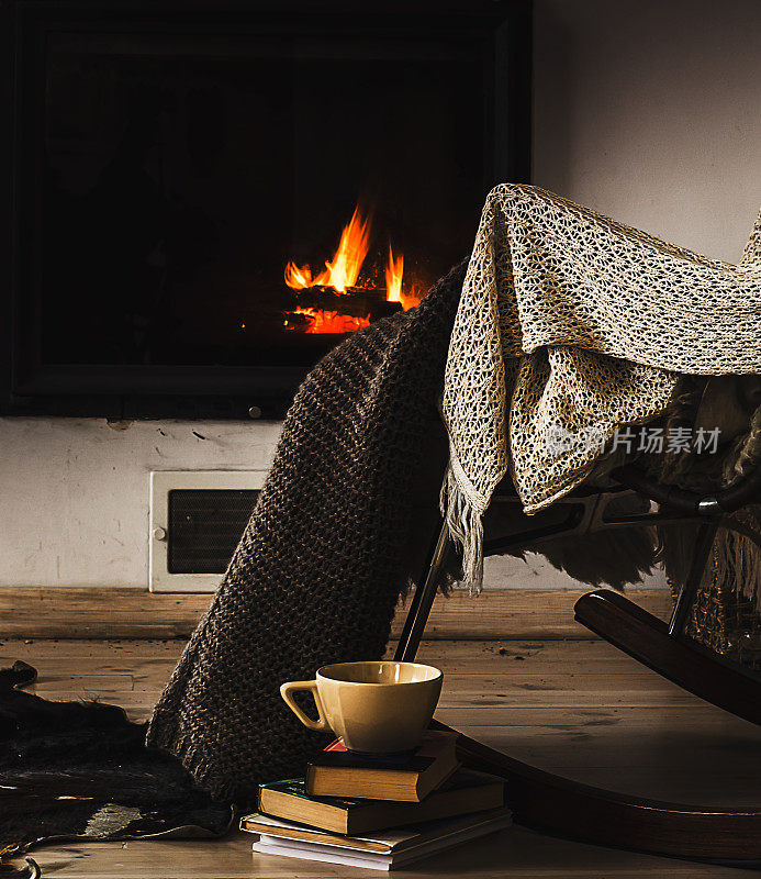 壁炉前的摇椅、针织地毯、书籍和一杯茶或咖啡