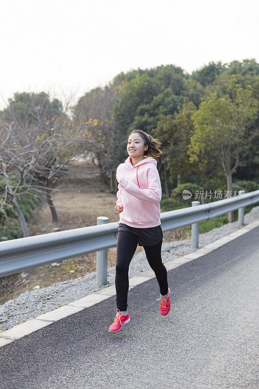 年轻女子在柏油路上伴着音乐奔跑