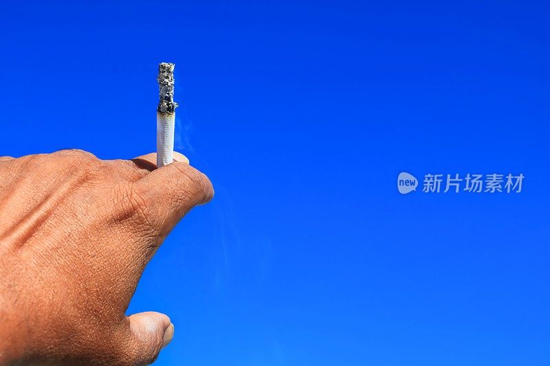 手握燃烧香烟在危险中，天空的背景。健康概念一天停止吸烟全世界。