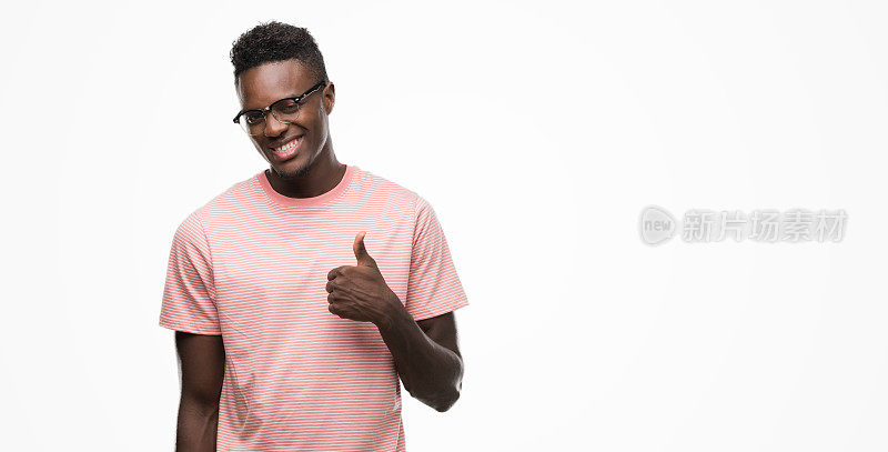 年轻的非洲裔美国人穿着粉红色的t恤做快乐的拇指手势与手。赞许的表情看着镜头，表示成功。