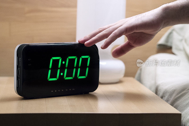 凌晨0点，一名男子试图关掉数字闹钟。