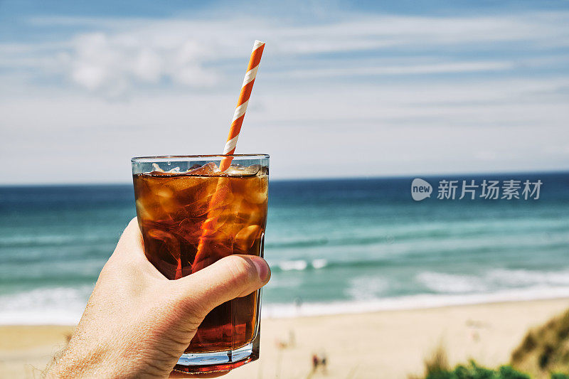 在一个炎热阳光明媚的夏日，手拿一杯冰黑咖啡在纽基的菲斯特拉海滩上。