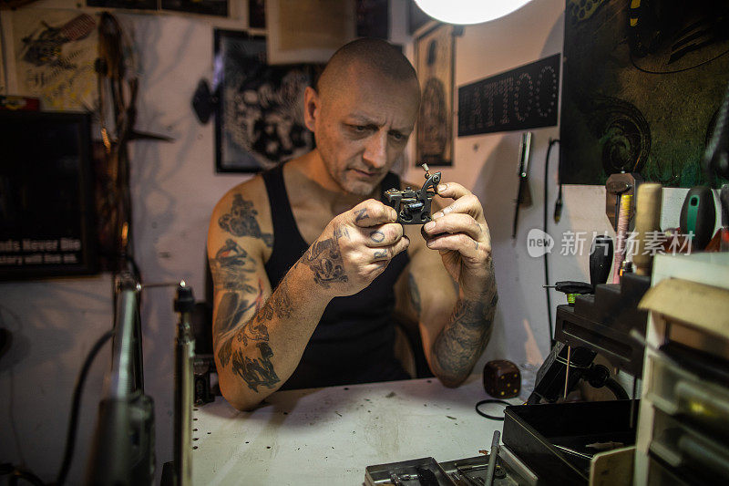 纹身艺术家坐在他的工作台上，看着他的纹身机