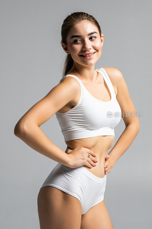 年轻美丽的女人身体在灰色的背景在白色运动服