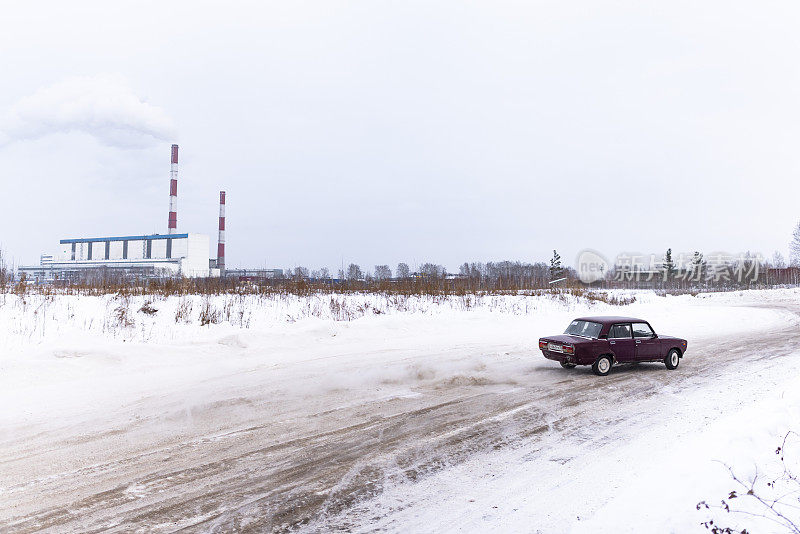 俄罗斯低红色汽车“VAZ-Zhiguli”在冬天的雪地里，在热电厂管道前的一个弯道上快速漂移。