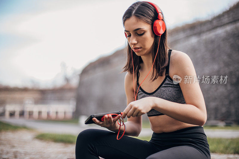 一个十几岁的女孩穿着运动服坐在长椅上听音乐