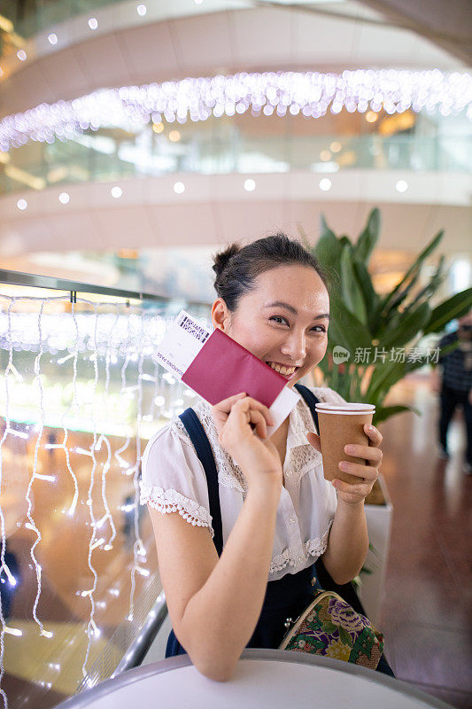 手持护照和登机牌的年轻女子在机场咖啡厅的肖像