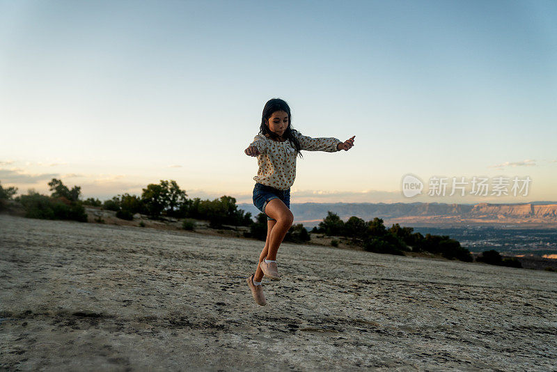 美丽的西班牙混血10岁女孩与长棕色头发做一个侧手翻岩石景观在科罗拉多附近的Fruita