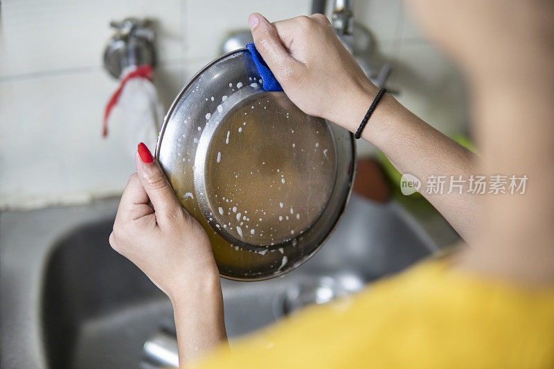 特写女人的手在厨房水槽上洗盘子。