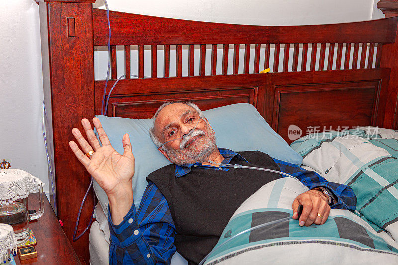 一名72岁的印度男子做完腹腔镜胆囊手术后躺在家中的床上恢复。他微笑着向镜头挥手致意。