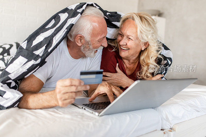 一对老年夫妇在床上用笔记本电脑网购
