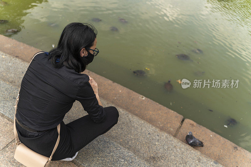 一个少女在曼哈顿中央公园的池塘里看乌龟。由于新冠肺炎疫情，她戴着安全口罩。