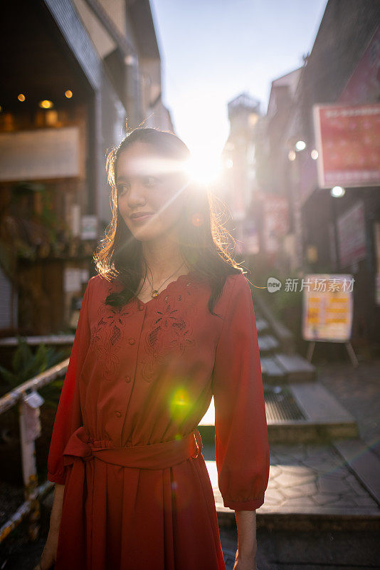 日落时分，年轻女子穿着红色裙子走在城市的台阶上