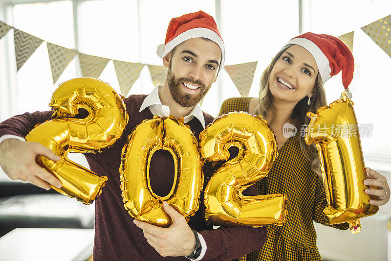 年轻夫妇在家庆祝新年，手持数字为2021的气球，代表即将到来的新年