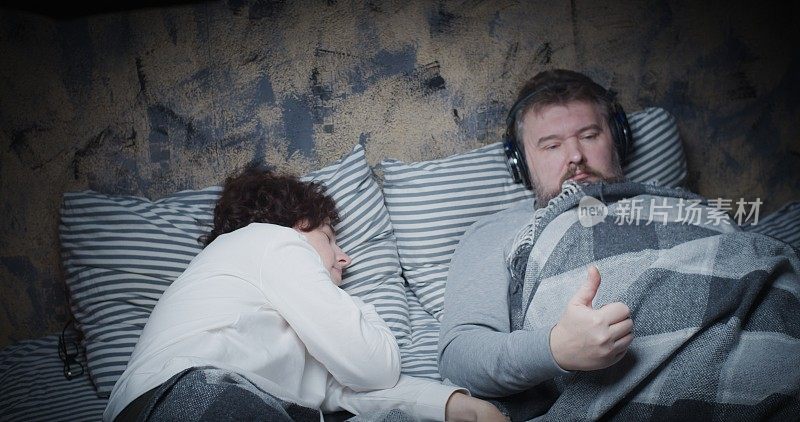 成熟的丈夫在床上听音乐，而妻子正在睡觉