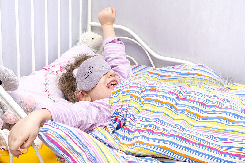 一个5岁的白人小孩，在婴儿床上伸展四肢。戴着面具睡觉的女孩。宝宝早上