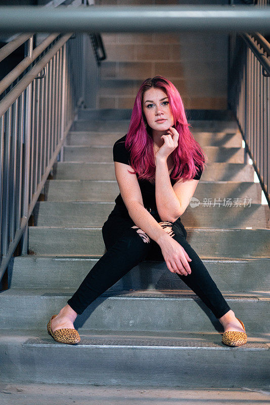 时尚，严肃的年轻女人与有趣可爱的亮粉色染发坐在楼梯室内