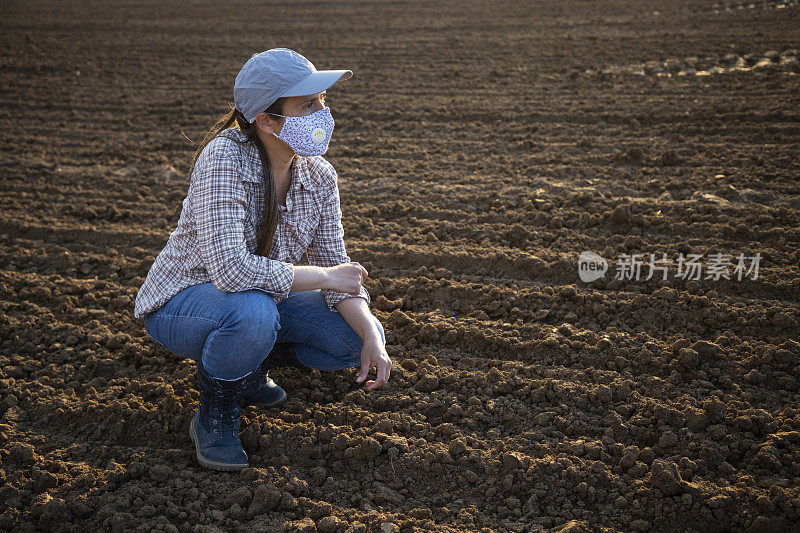 在2019冠状病毒病大流行期间，为作物施肥的农民在结束一天的工作时，戴着防护口罩的农民望向别处。