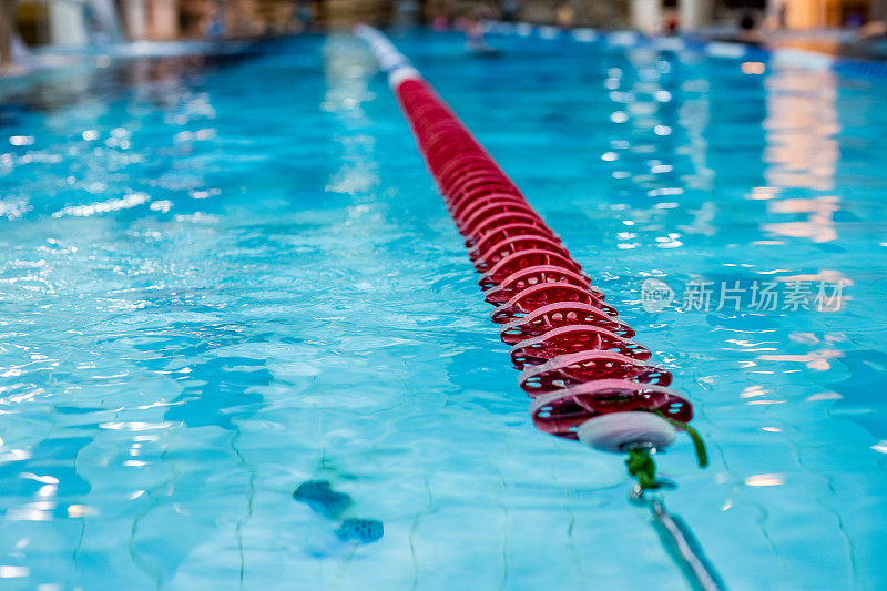泳池内红色泳道标志。不褪色的游泳池泳道线。游泳池的泳道绳索。红色塑料绳巷在蓝水室内游泳池体育比赛的背景。有选择性的重点