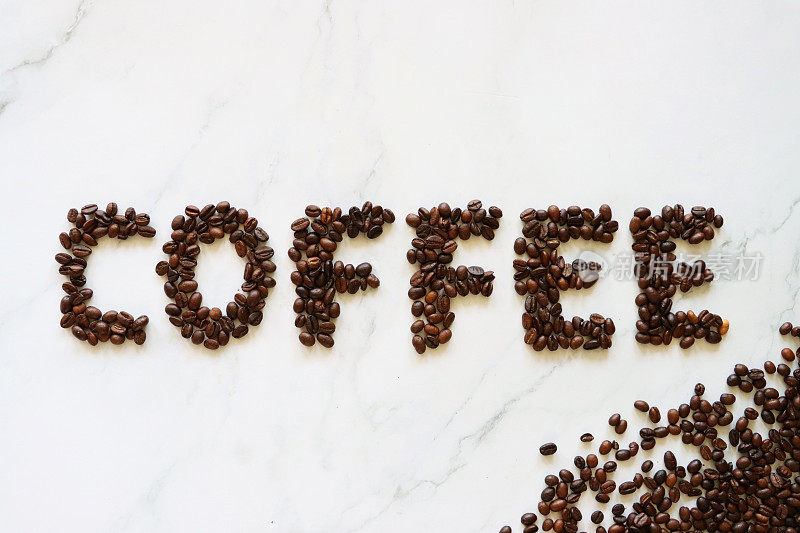 在大理石效果的背景上，在一小堆烘烤过的咖啡豆旁边，用整颗咖啡豆写的“咖啡”一词的图像