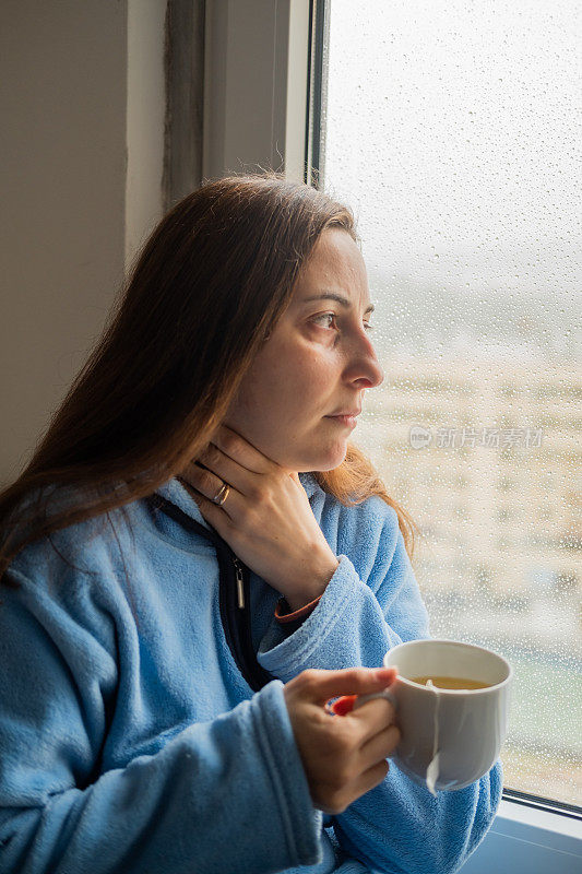 一个喉咙痛的女人在窗外喝茶，外面下雨了