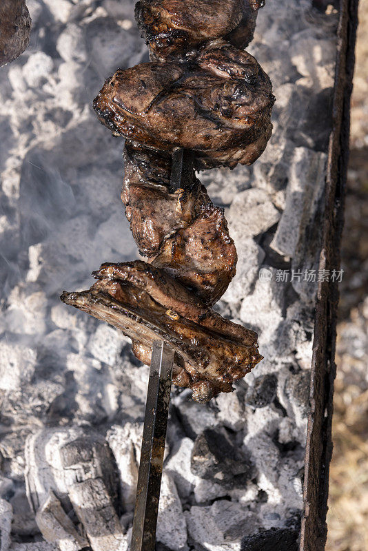 垂直特写，几块串好的羊肉正在烹饪，缕缕白烟从覆盖着灰烬的木炭中升起