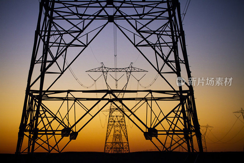 在西南沙漠，一排输电塔的剪影映衬着橙色的夕阳天空