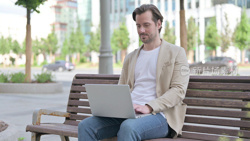 年轻人坐在长凳上使用笔记本电脑