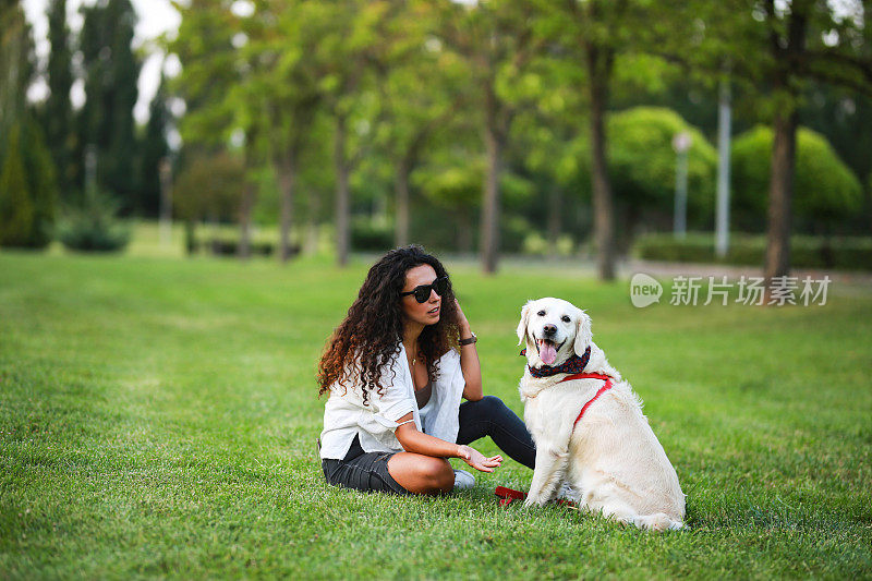 美丽的
深色头发的女人有一个很好的时间和她的金色拉布拉多寻回狗在公园的草地上日落。动物的爱