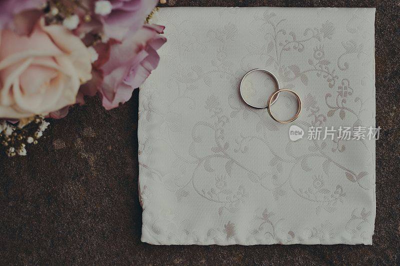 顶视图的金婚戒指上的白色织物由美丽的玫瑰花束