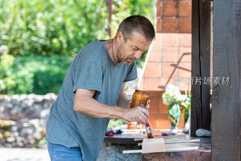 在阳光明媚的日子里，男人正在为家里的露台粉刷木板